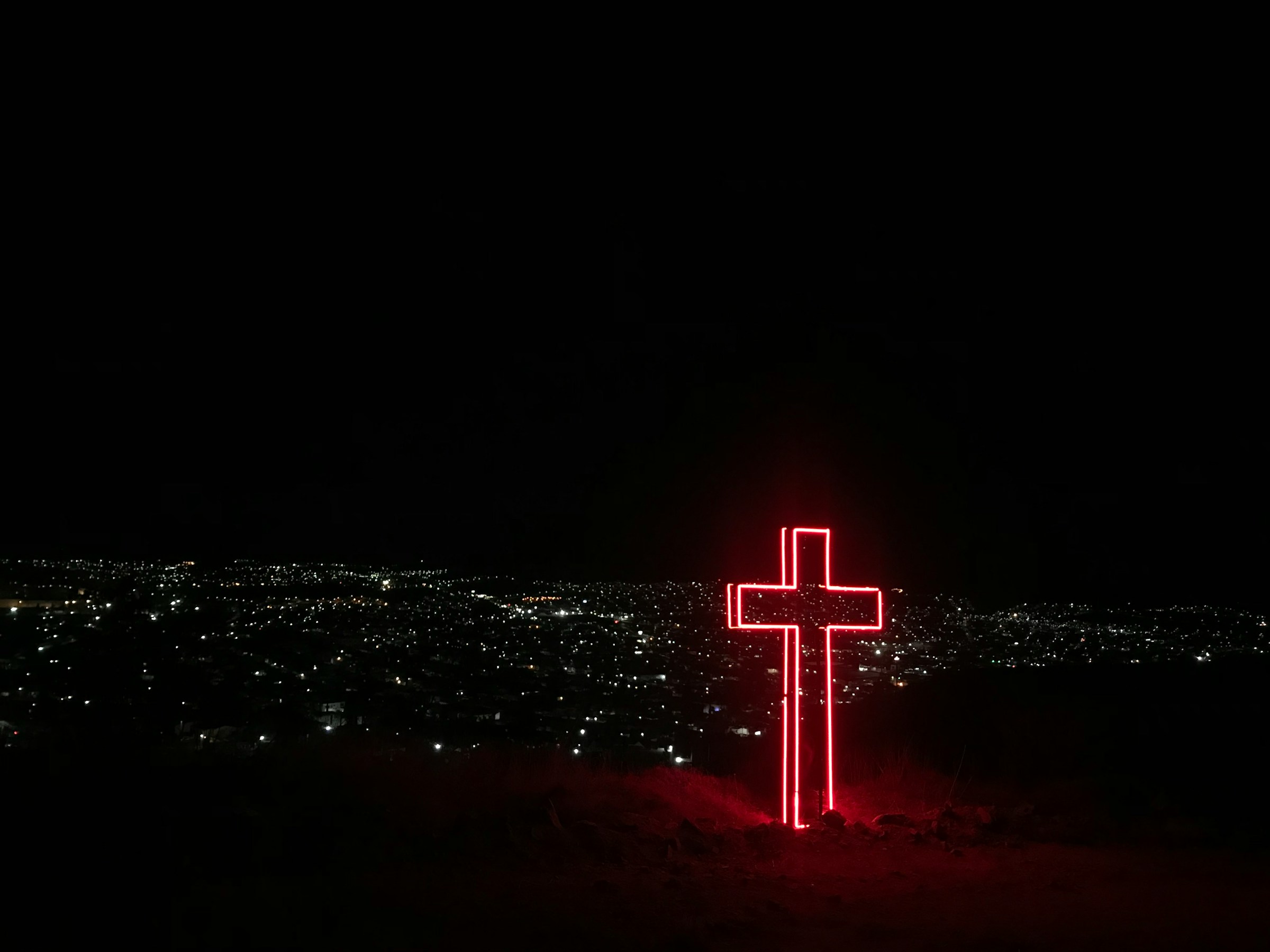Red neon cross outside city on night